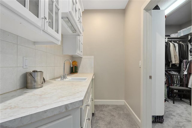 interior space featuring light carpet, white cabinets, decorative backsplash, light countertops, and a sink