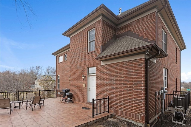 view of home's exterior with a patio, brick siding, and roof with shingles