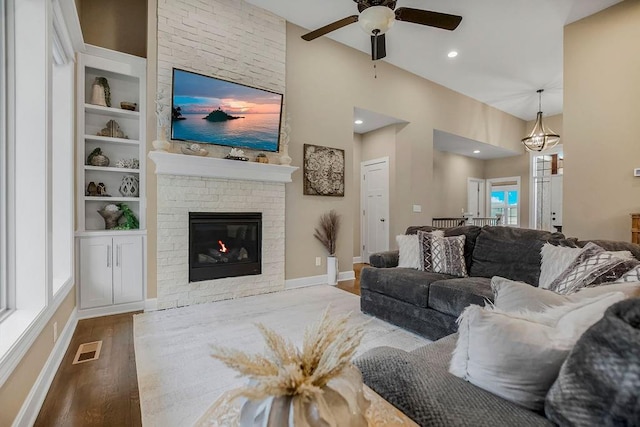 living room featuring a brick fireplace, built in shelves, ceiling fan, and light hardwood / wood-style flooring