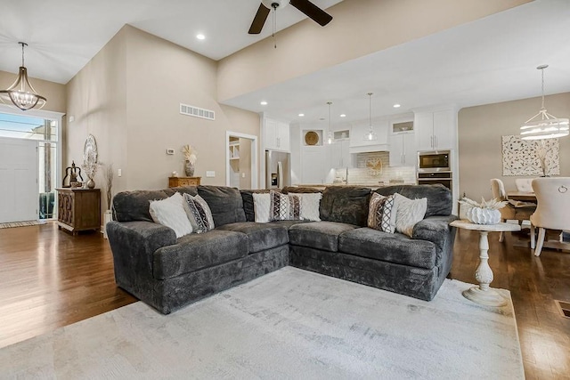 living room with dark hardwood / wood-style floors, ceiling fan with notable chandelier, and a high ceiling