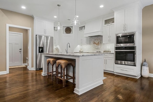 kitchen featuring decorative light fixtures, stainless steel appliances, white cabinets, and a center island with sink