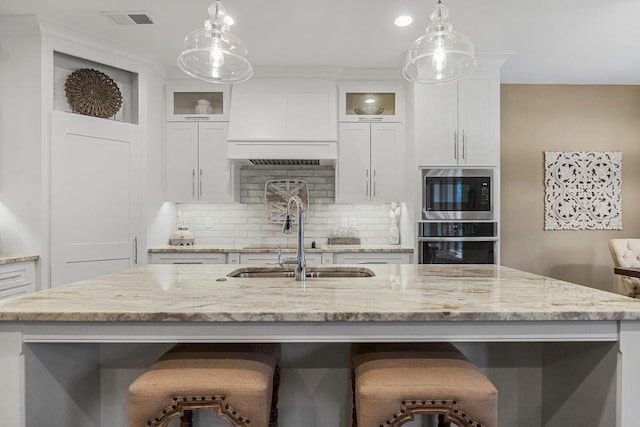 kitchen featuring built in microwave, decorative light fixtures, oven, and an island with sink