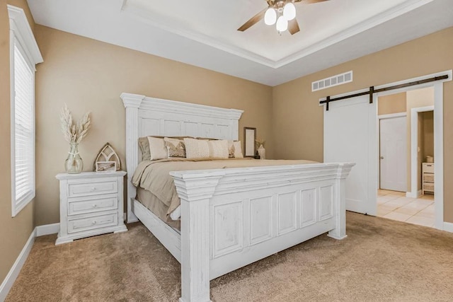 bedroom featuring light colored carpet, a barn door, a raised ceiling, and multiple windows