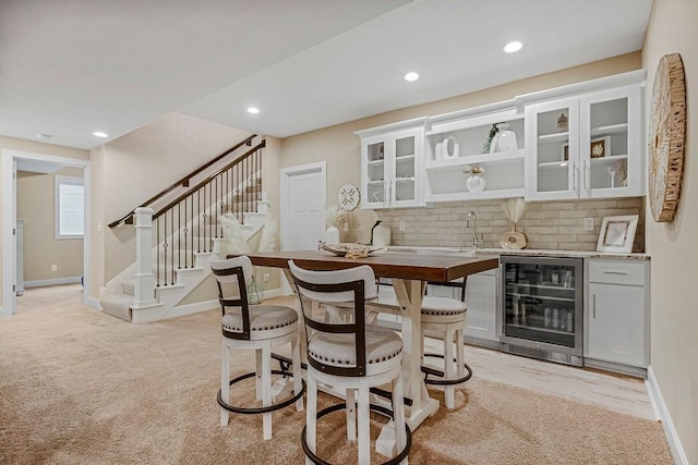 bar with white cabinets, light colored carpet, wine cooler, and backsplash