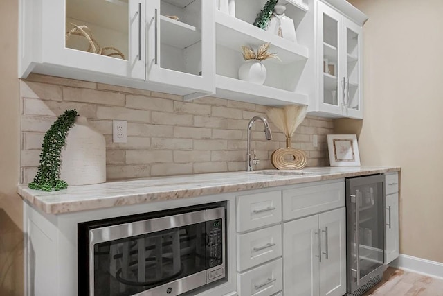 bar with sink, white cabinetry, backsplash, light stone countertops, and beverage cooler