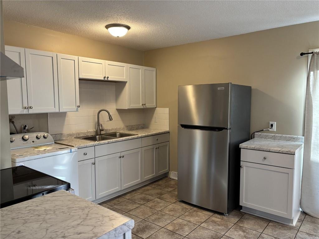 kitchen featuring light countertops, a sink, freestanding refrigerator, and white cabinets