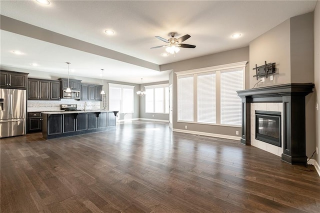 unfurnished living room featuring dark wood-type flooring, a tile fireplace, and ceiling fan with notable chandelier