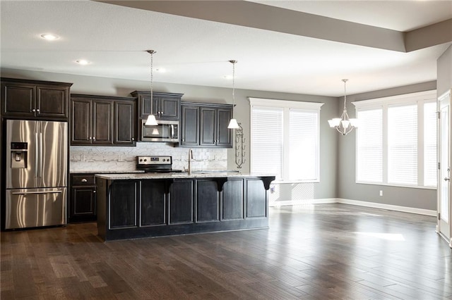 kitchen featuring tasteful backsplash, hanging light fixtures, stainless steel appliances, dark hardwood / wood-style floors, and a kitchen island with sink