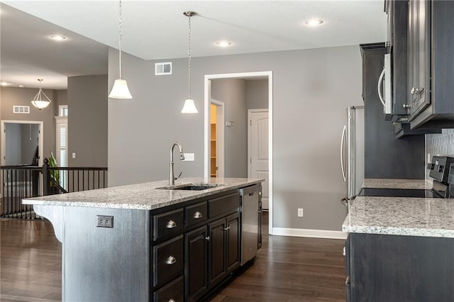 kitchen with appliances with stainless steel finishes, light stone counters, decorative light fixtures, sink, and a kitchen island with sink