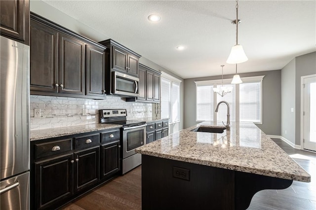 kitchen with a center island with sink, stainless steel appliances, sink, backsplash, and pendant lighting