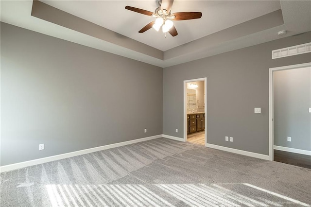 unfurnished bedroom with light carpet, ceiling fan, ensuite bath, and a tray ceiling