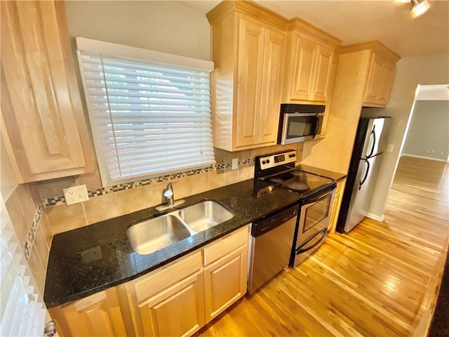 kitchen featuring light brown cabinetry, sink, light wood-type flooring, dark stone countertops, and stainless steel appliances