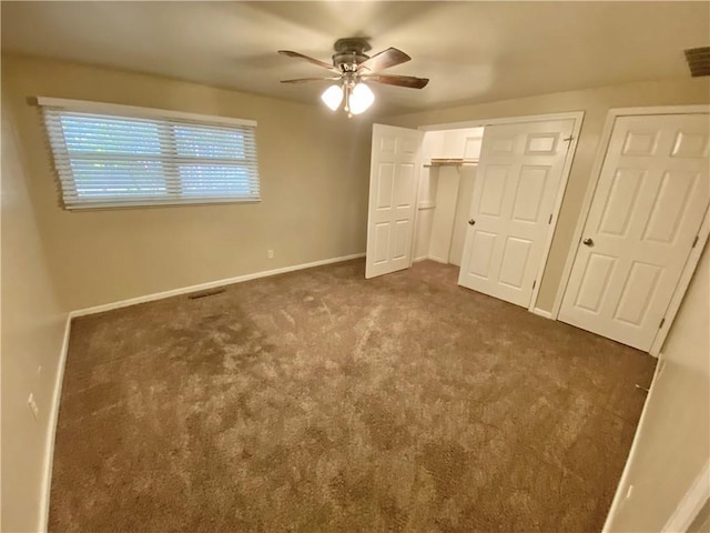 unfurnished bedroom with dark colored carpet, two closets, and ceiling fan