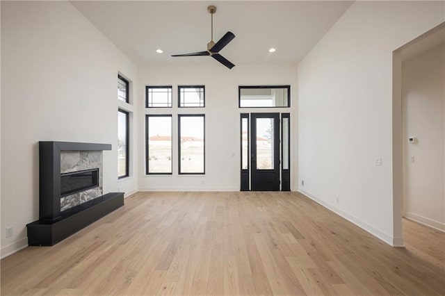 unfurnished living room featuring a wealth of natural light, a premium fireplace, ceiling fan, and light wood-type flooring