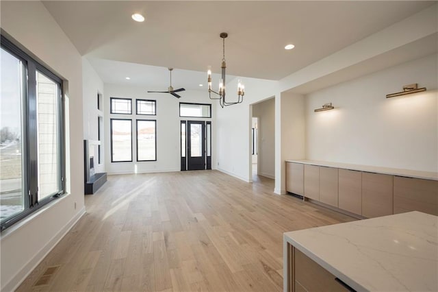 interior space with ceiling fan with notable chandelier, a wealth of natural light, and light hardwood / wood-style flooring