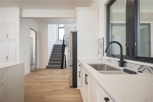 kitchen with sink, stainless steel refrigerator, light stone countertops, white cabinets, and light wood-type flooring