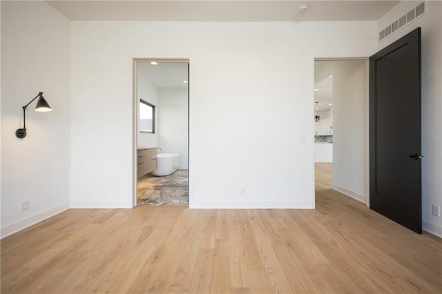 unfurnished bedroom with ensuite bathroom and light hardwood / wood-style floors