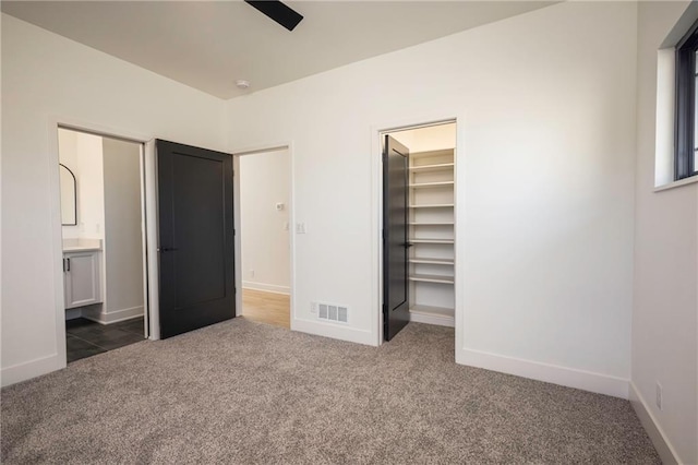 unfurnished bedroom with a walk in closet, ensuite bathroom, dark carpet, and a closet