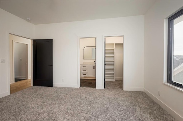 unfurnished bedroom with ensuite bath, a walk in closet, a closet, and carpet