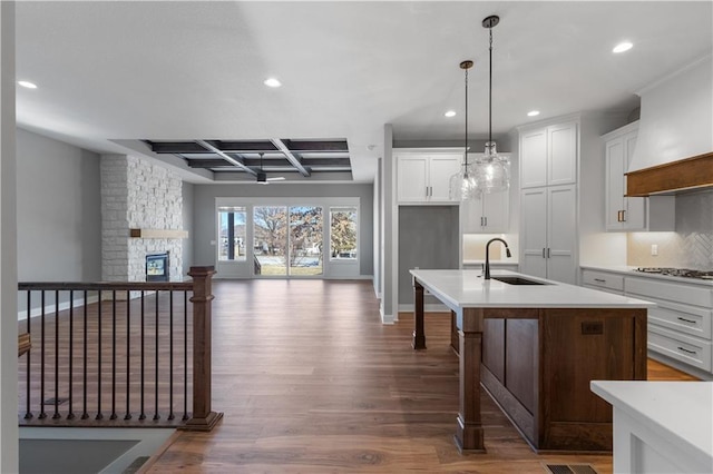 kitchen featuring coffered ceiling, sink, white cabinetry, decorative light fixtures, and an island with sink