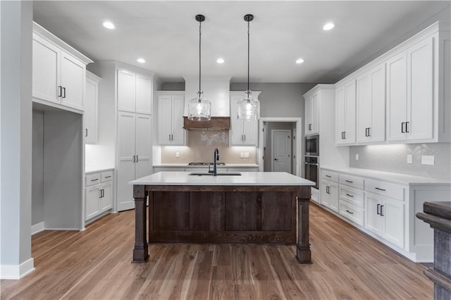 kitchen with a kitchen island with sink, pendant lighting, white cabinets, and appliances with stainless steel finishes