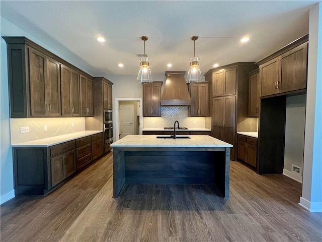 17178 S Heatherwood St, Olathe, KS 66062 - kitchen with custom exhaust hood, a center island with sink, tasteful backsplash, dark wood-style flooring, and recessed lighting