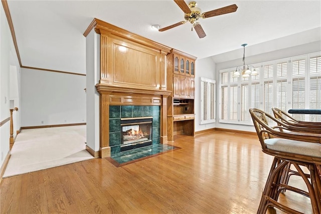 unfurnished living room with a tiled fireplace, ceiling fan with notable chandelier, and light hardwood / wood-style flooring