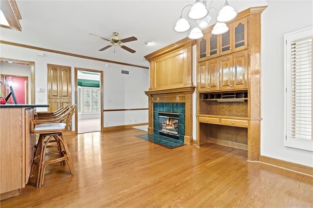 living room featuring a tiled fireplace, ceiling fan with notable chandelier, light hardwood / wood-style flooring, and ornamental molding