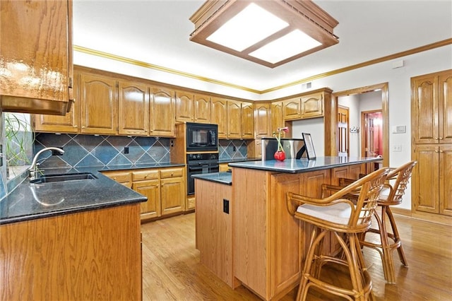 kitchen featuring sink, a kitchen bar, a center island, black appliances, and light wood-type flooring