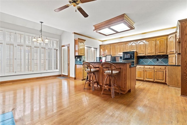 kitchen with pendant lighting, a kitchen breakfast bar, black microwave, and light hardwood / wood-style flooring