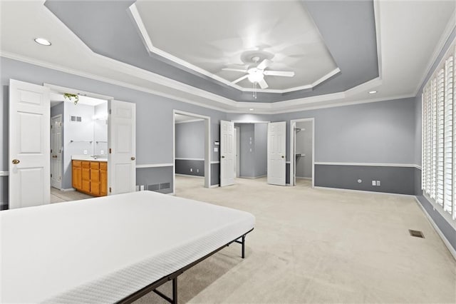 bedroom featuring ensuite bath, ceiling fan, ornamental molding, light colored carpet, and a raised ceiling