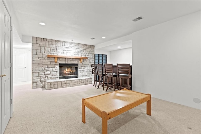 living room with a stone fireplace, light carpet, and indoor bar