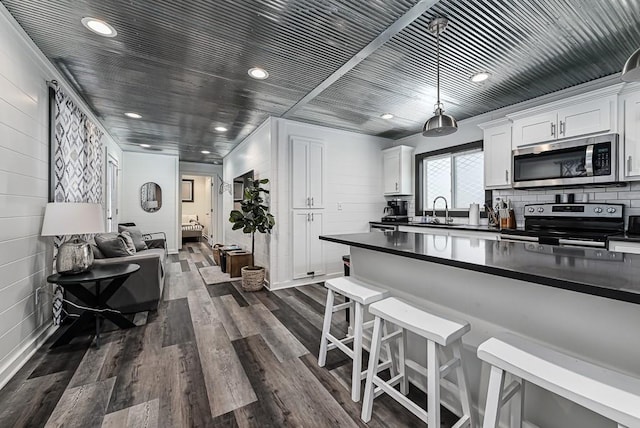 kitchen featuring pendant lighting, white cabinetry, a kitchen bar, stainless steel appliances, and dark wood-type flooring