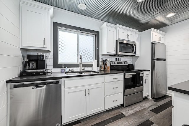 kitchen with sink, appliances with stainless steel finishes, wooden walls, white cabinets, and backsplash