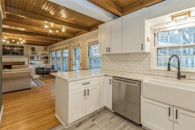 kitchen featuring sink, white cabinetry, a brick fireplace, stainless steel dishwasher, and kitchen peninsula