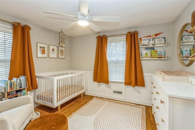 bedroom with a nursery area, ceiling fan, multiple windows, and light wood-type flooring