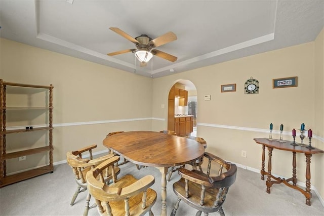 dining area featuring a tray ceiling, arched walkways, a ceiling fan, light carpet, and baseboards