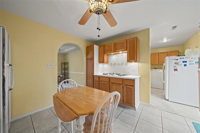 kitchen with arched walkways, light tile patterned floors, white appliances, tasteful backsplash, and washer / dryer