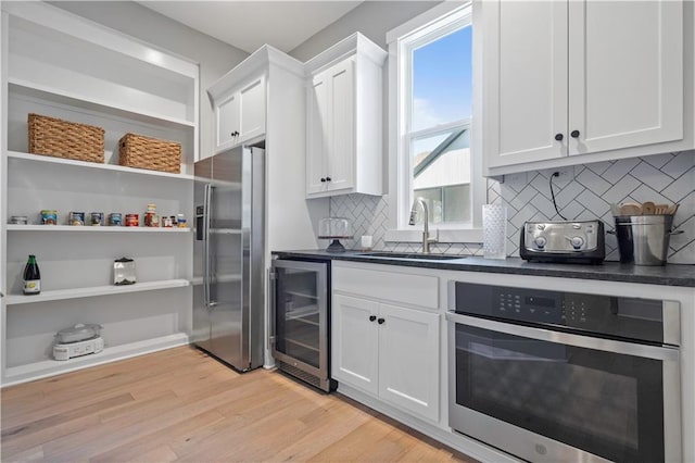 kitchen featuring wine cooler, dark countertops, appliances with stainless steel finishes, white cabinets, and a sink