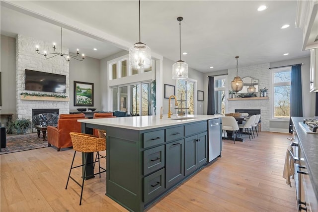 kitchen featuring open floor plan, a stone fireplace, an island with sink, and a sink