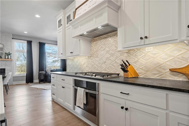 kitchen with appliances with stainless steel finishes, white cabinets, premium range hood, and glass insert cabinets