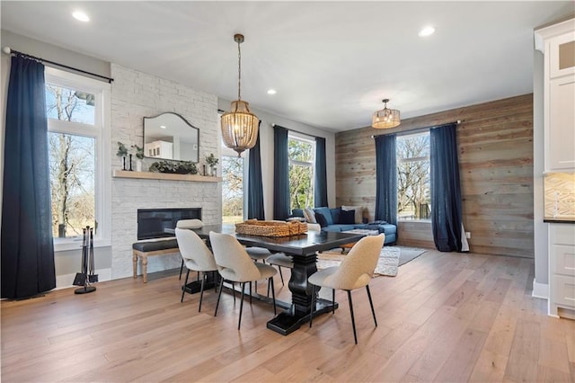 dining room featuring light wood finished floors, wood walls, a fireplace, and recessed lighting