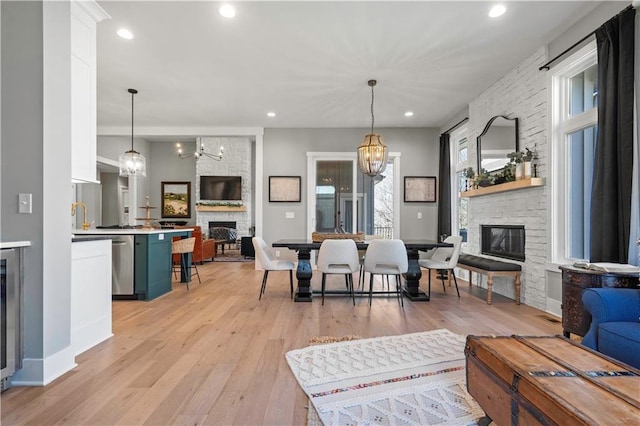 living room featuring light wood-type flooring, a healthy amount of sunlight, a fireplace, and an inviting chandelier