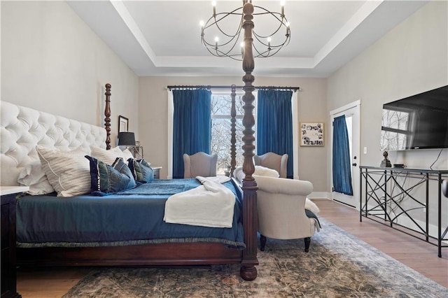 bedroom featuring a chandelier, a tray ceiling, baseboards, and wood finished floors