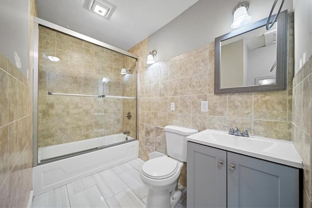 full bathroom with toilet, shower / bath combination with glass door, tile walls, a textured ceiling, and vanity