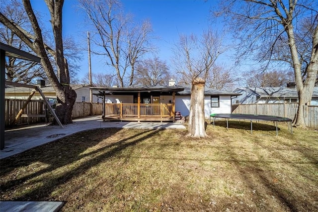 rear view of property featuring a deck, a yard, and a trampoline