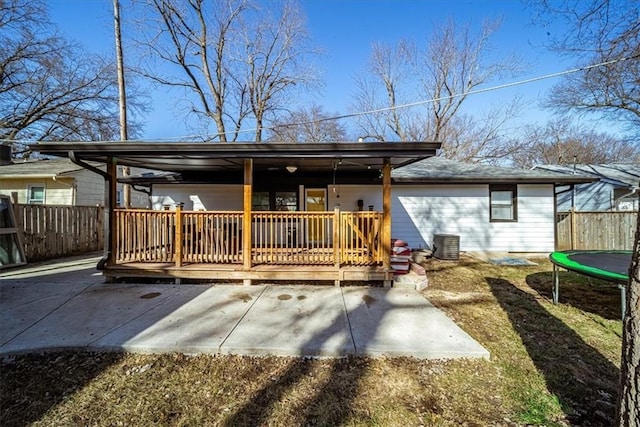 back of property featuring a trampoline, a wooden deck, and a patio area