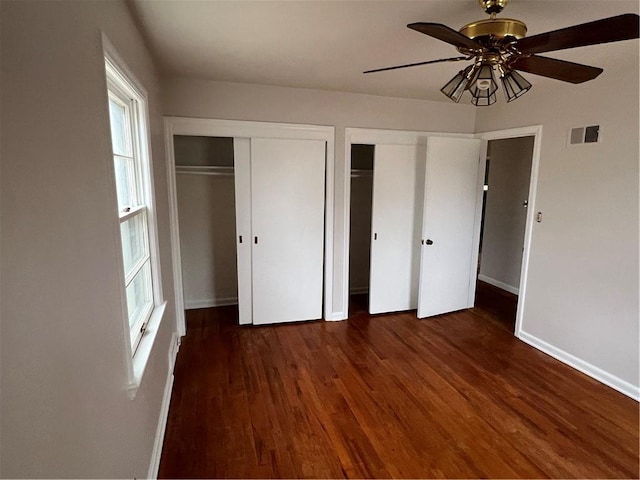 unfurnished bedroom featuring multiple closets, ceiling fan, and dark wood-type flooring