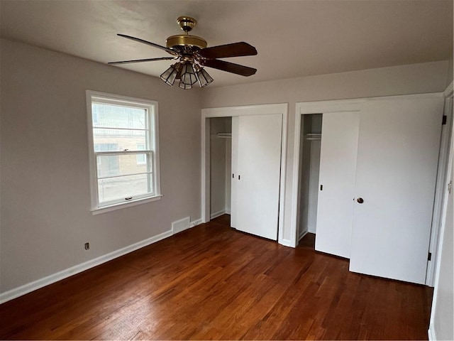 unfurnished bedroom featuring dark hardwood / wood-style flooring, ceiling fan, and multiple closets