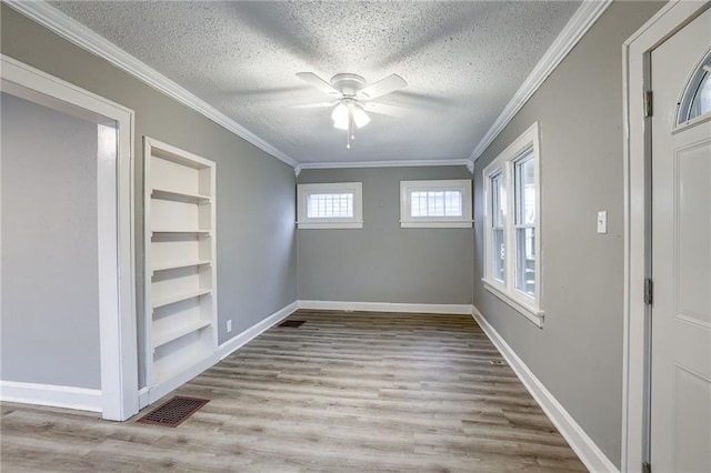 empty room with ornamental molding, light hardwood / wood-style flooring, a textured ceiling, and built in shelves